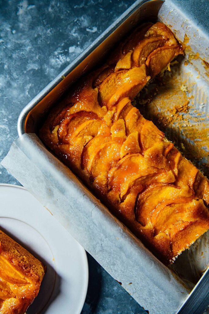 peach cardamom and saffron cake sliced in the baking pan with peach slices on top