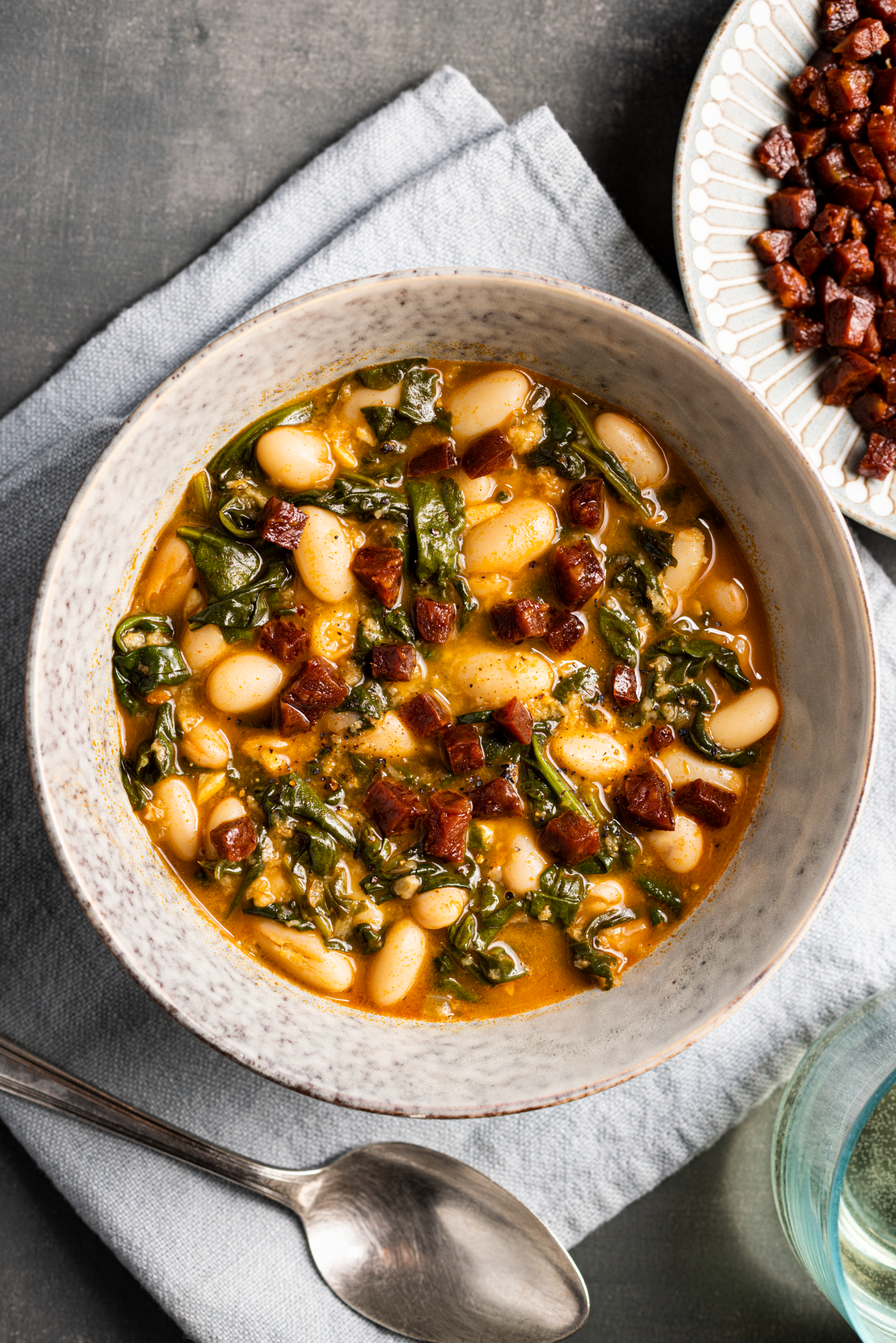Chorizo and white bean soup in a bowl with crispy sausage and spinach, showing the science of flavor layering.