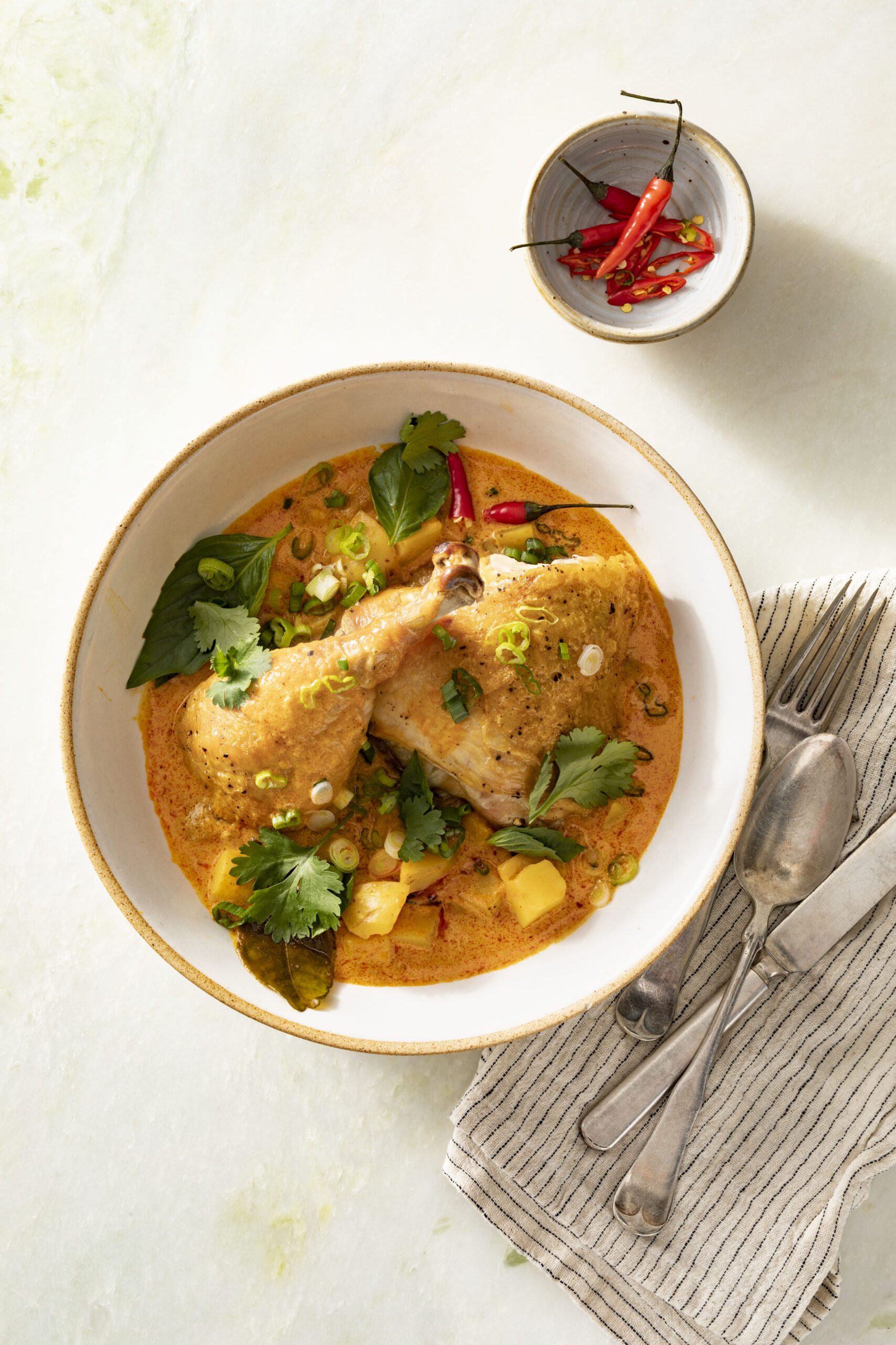 Spatchcocked roast chicken served over kabocha squash and potatoes in a rich Thai red curry coconut sauce, garnished with Thai basil, cilantro, and sliced chiles