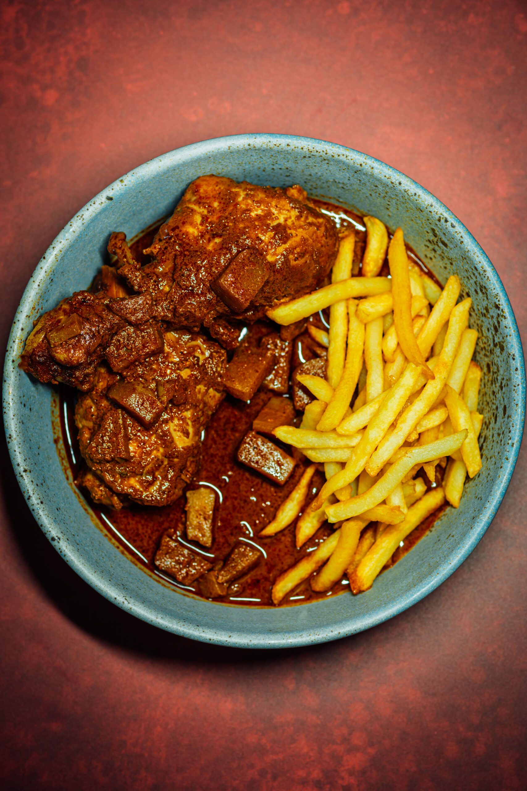 Bowl of chicken mole negro with chayote and crispy french fries in a blue ceramic bowl