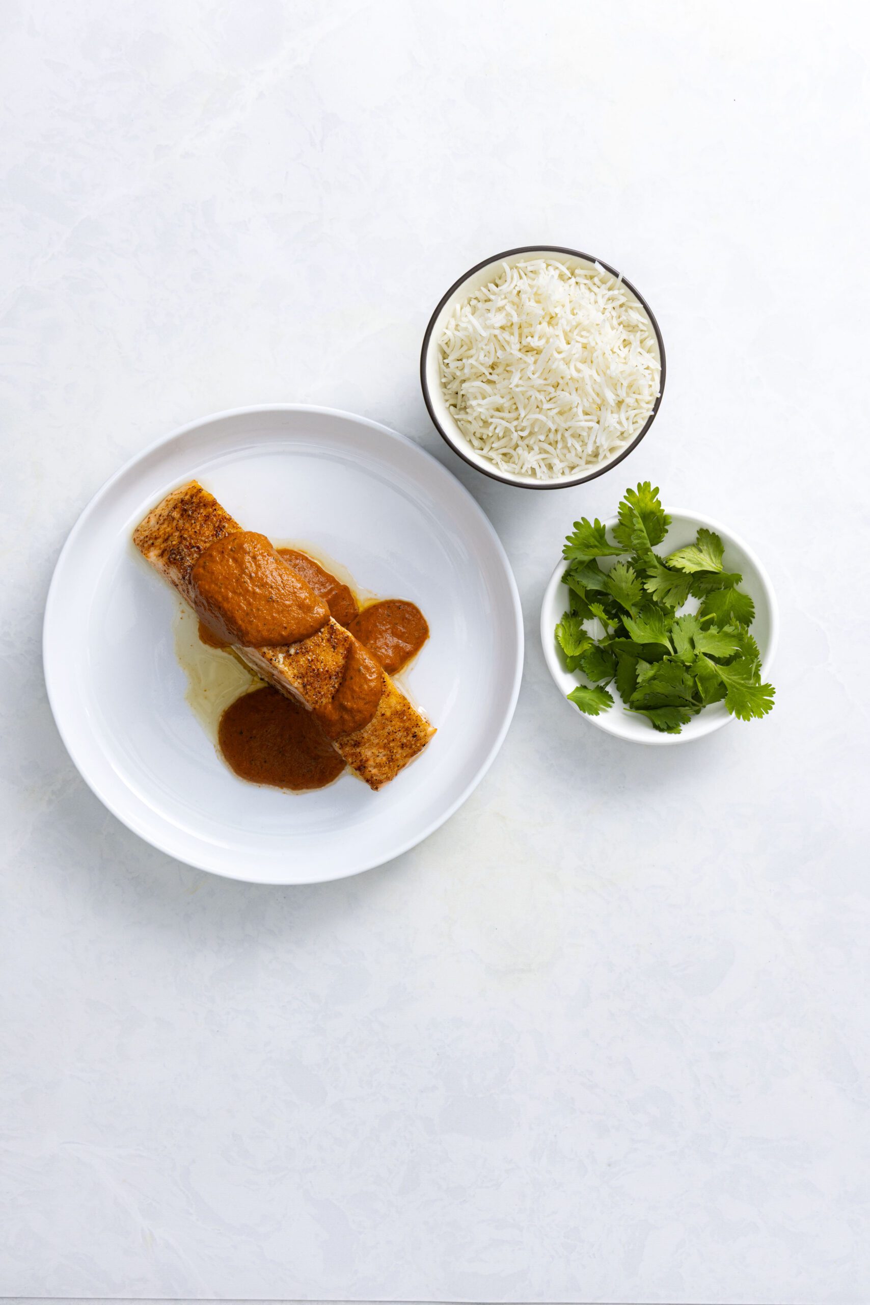Salmon tikka masala fillet with creamy Kashmiri masala sauce on a white plate, served with basmati rice and fresh cilantro