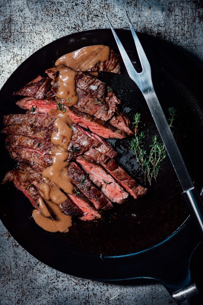 Sliced sous vide steak with a browned crust and porcini-thyme pan sauce served in a cast-iron skillet.