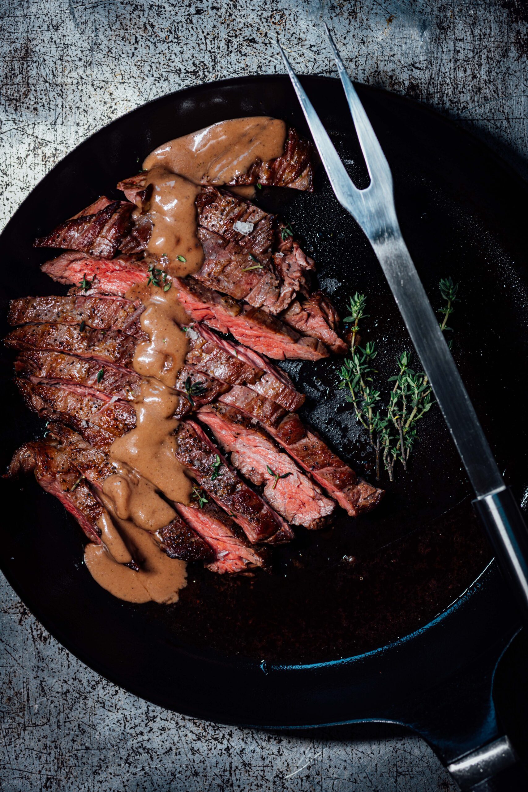 Sliced sous vide steak with a browned crust and porcini-thyme pan sauce served in a cast-iron skillet.