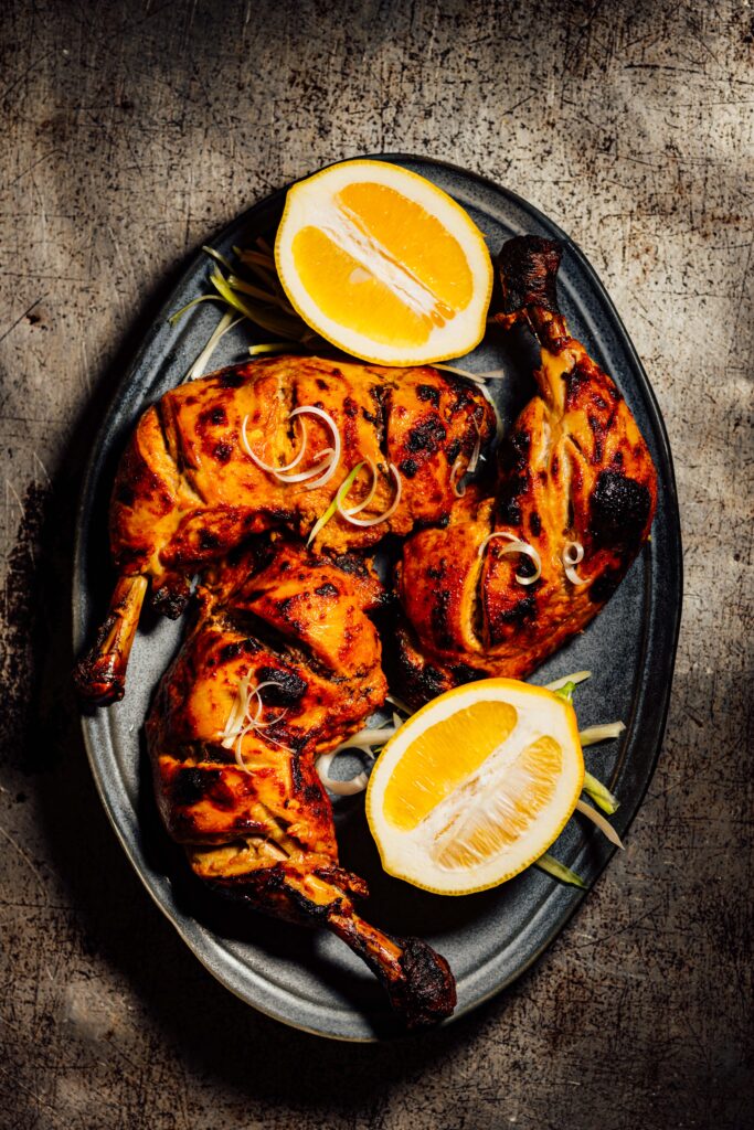 Charred tandoori chicken served with halved lemons on a platter.