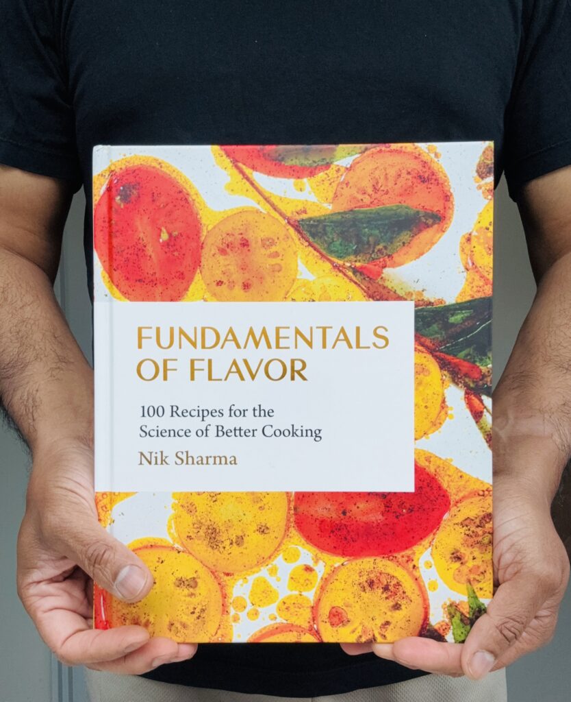 Fundamentals of Flavor cookbook by Nik Sharma held in two hands, cover featuring citrus and tomato slices